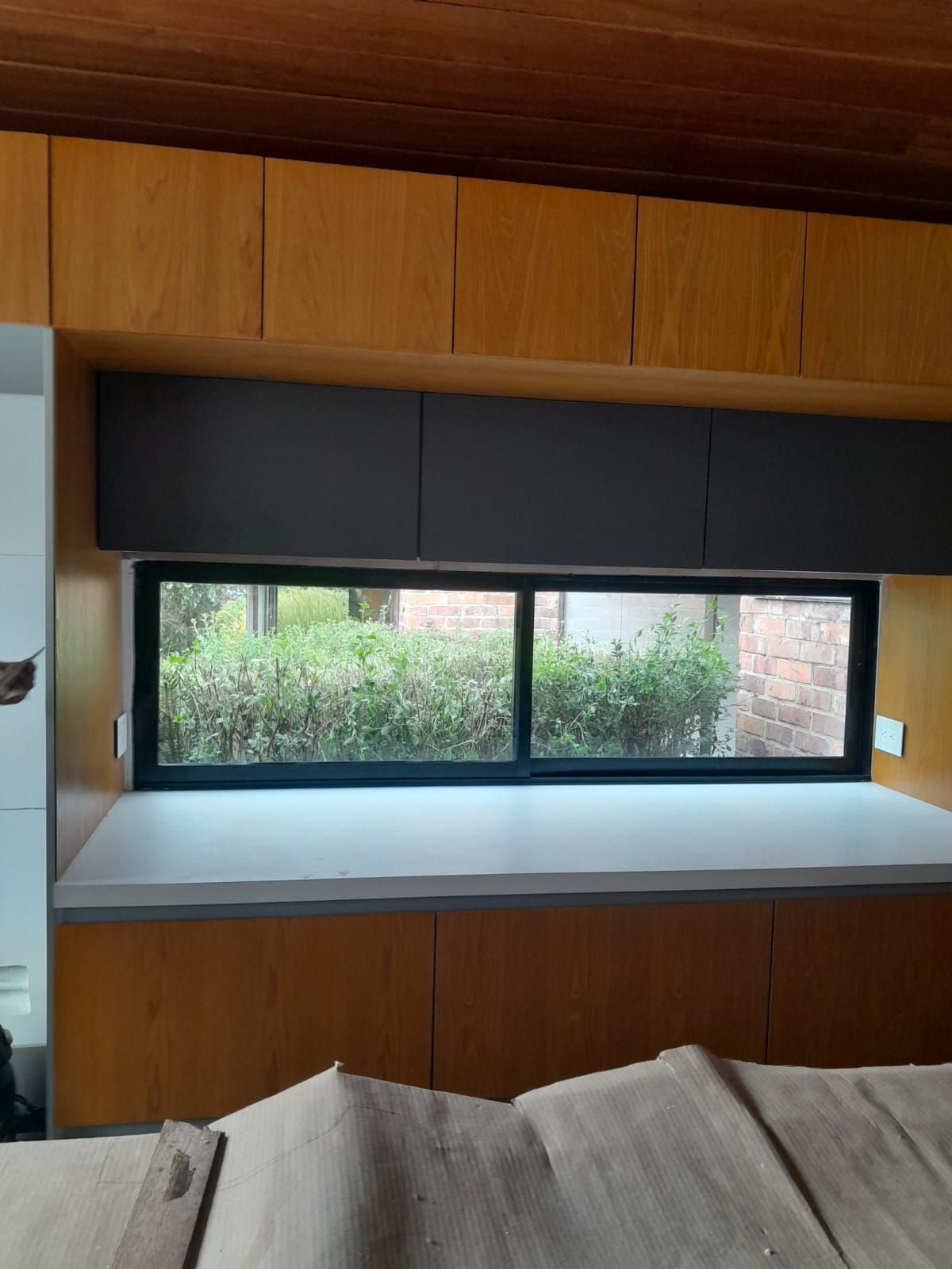 Asiento de ventana empotrado de madera, con armarios oscuros encima y vistas a la vegetación exterior