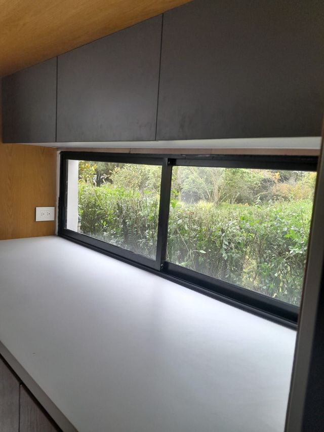 Rincón de escritorio minimalista con encimera blanca, armarios oscuros y una ventana amplia con vistas a la vegetación