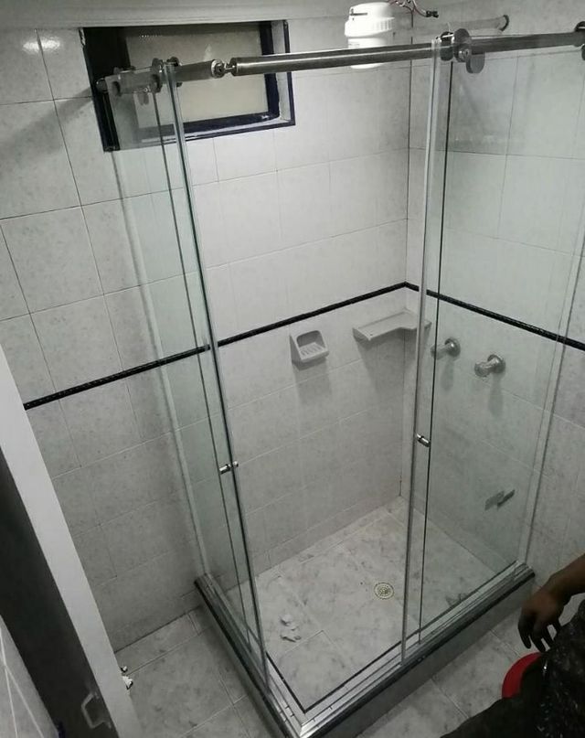 Mampara de ducha de cristal en un baño alicatado, con un cabezal de ducha y un pequeño estante en la pared.
