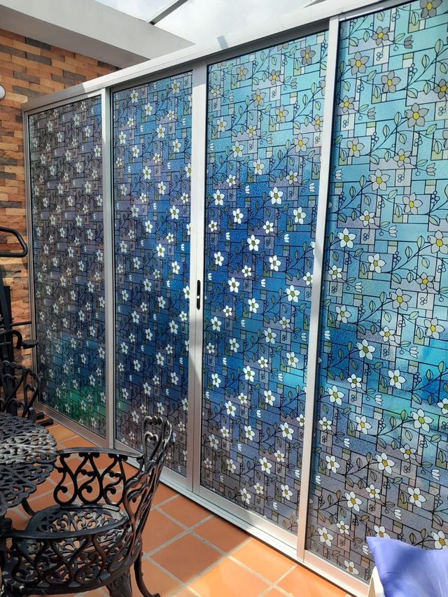 Biombo azul de cuatro paneles con estampado, en un patio embaldosado junto a unas sillas de hierro forjado.