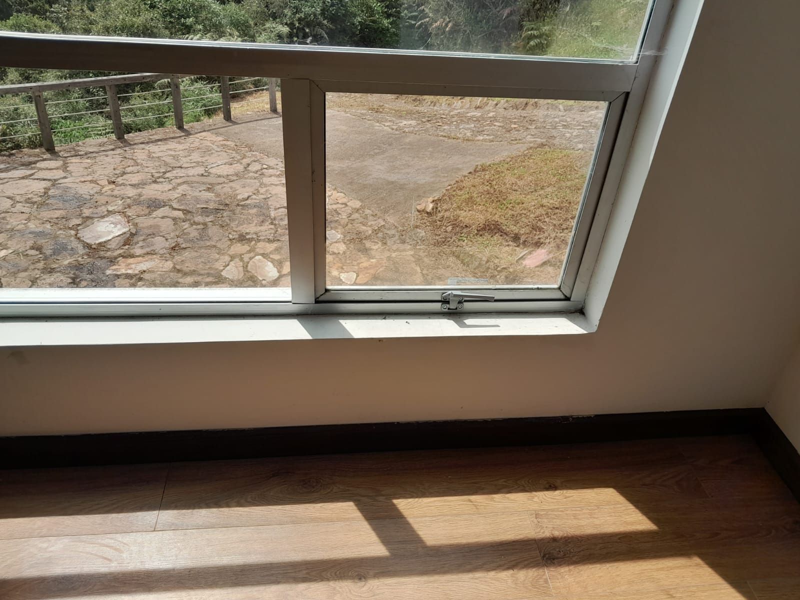 La luz del sol proyecta sombras de los cristales de la ventana sobre un suelo de madera junto a una ventana baja