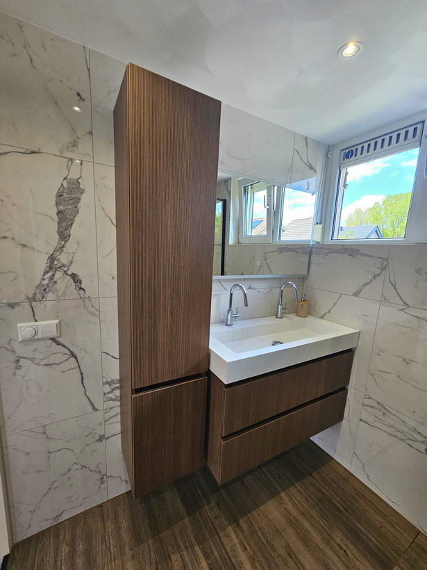 Moderne badkamermeubel met houten kastjes, marmerlookwanden, witte wastafel en uitzicht op het raam.
