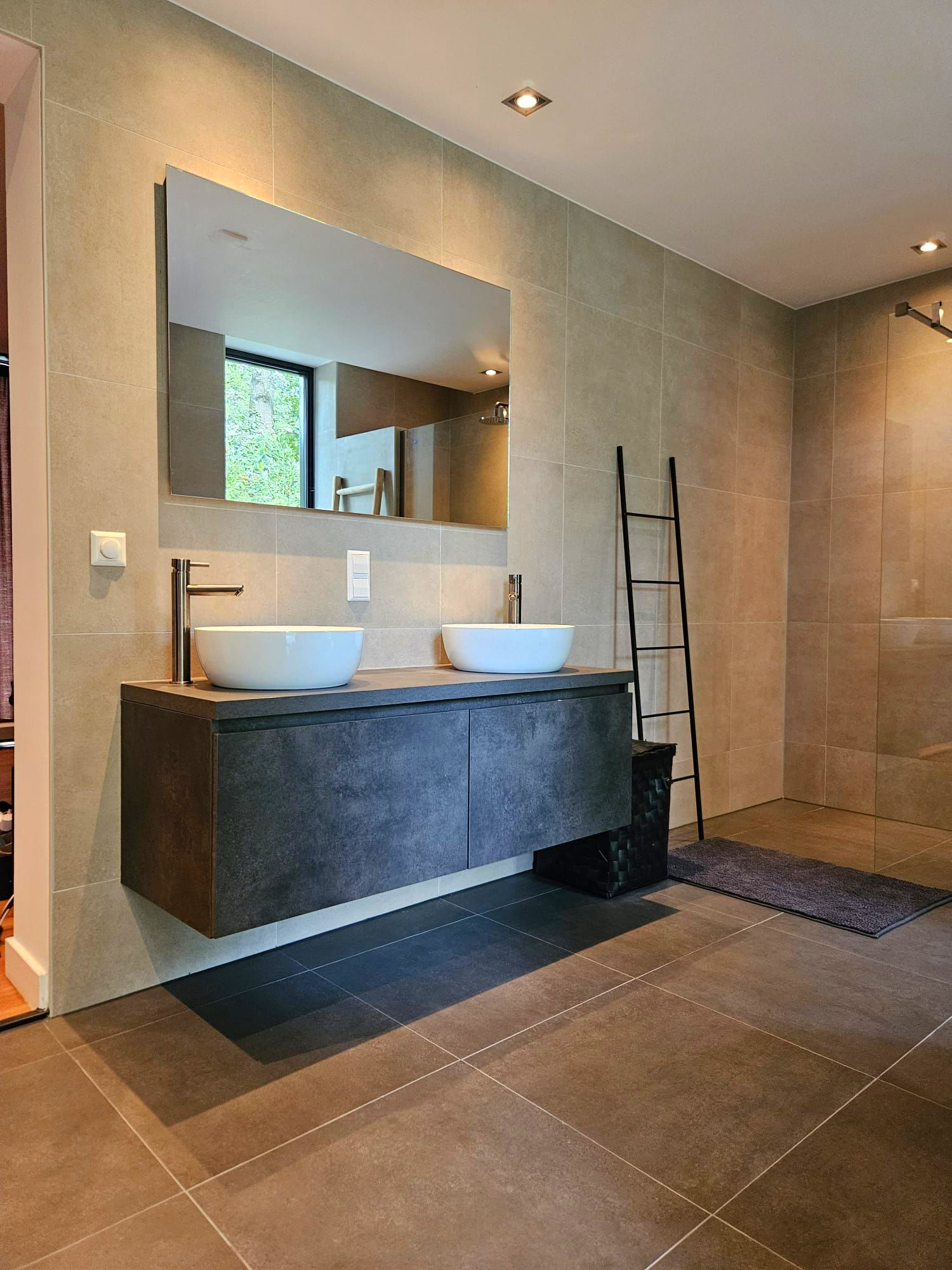 Moderne badkamer met een zwevend badkamermeubel met dubbele wastafel, grote spiegel, betegelde vloer en handdoekenrek in ladderstijl.