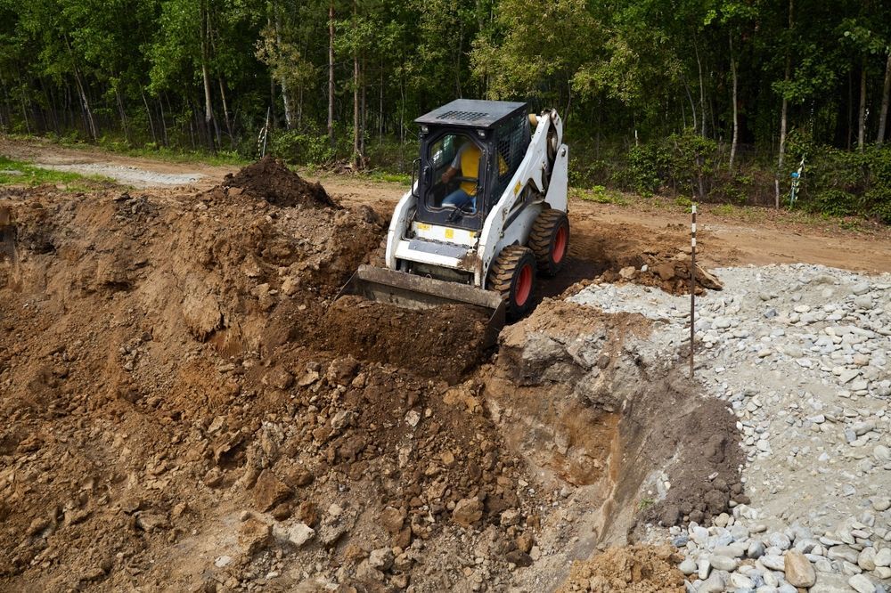 Small skid steer excavator on a dirt slope at a construction site near a wooded area