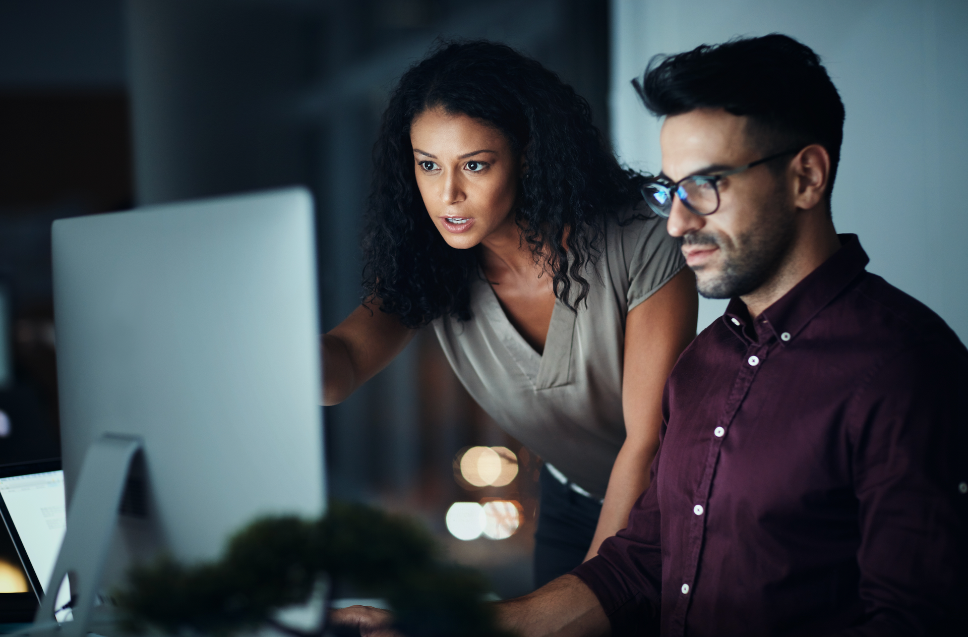 A man and a woman are looking at a computer screen at night.
