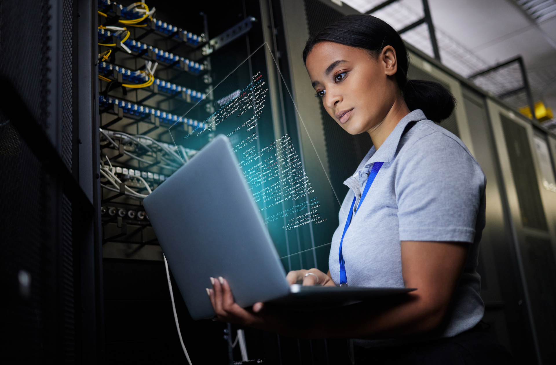 A woman is using a laptop computer in a server room.