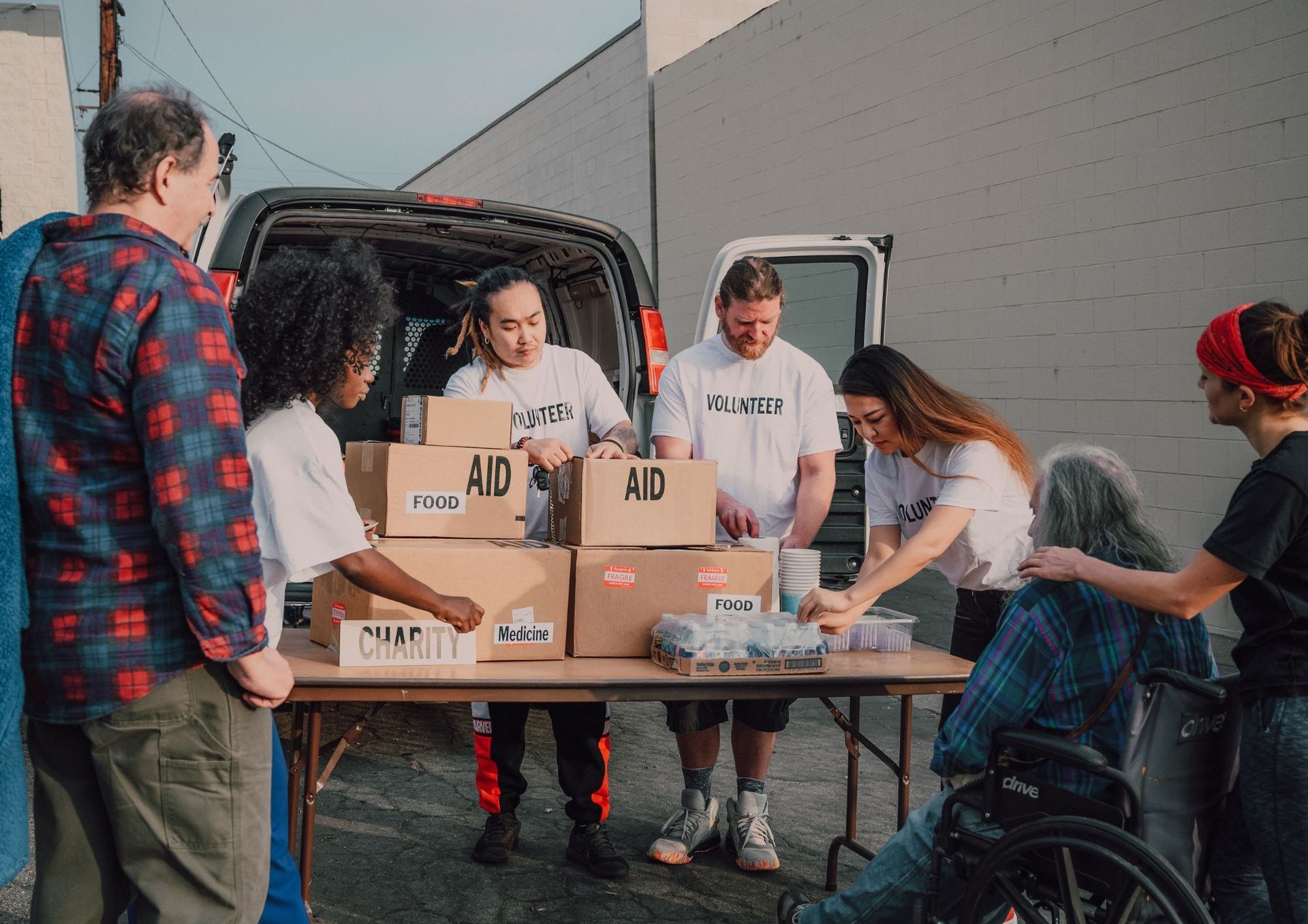 Volunteers packing boxes at a donation table beside a delivery van.