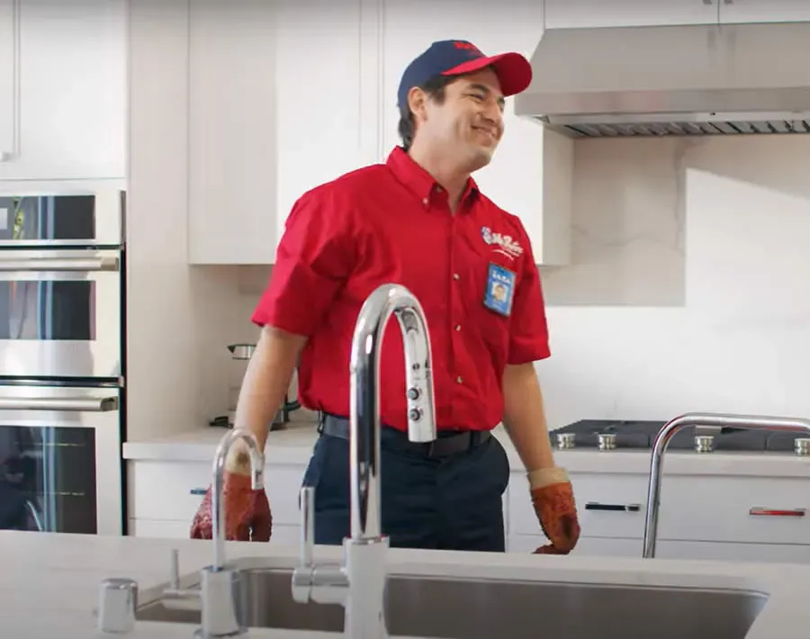 A professional wearing a red uniform and cap shows a tablet screen to a person while standing in a home.