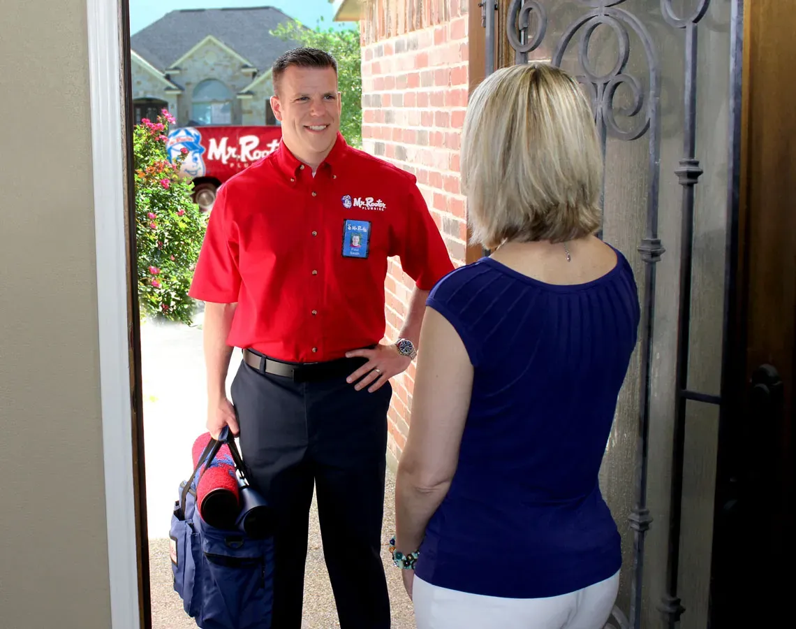 A professional wearing a red uniform and cap shows a tablet screen to a person while standing in a home.