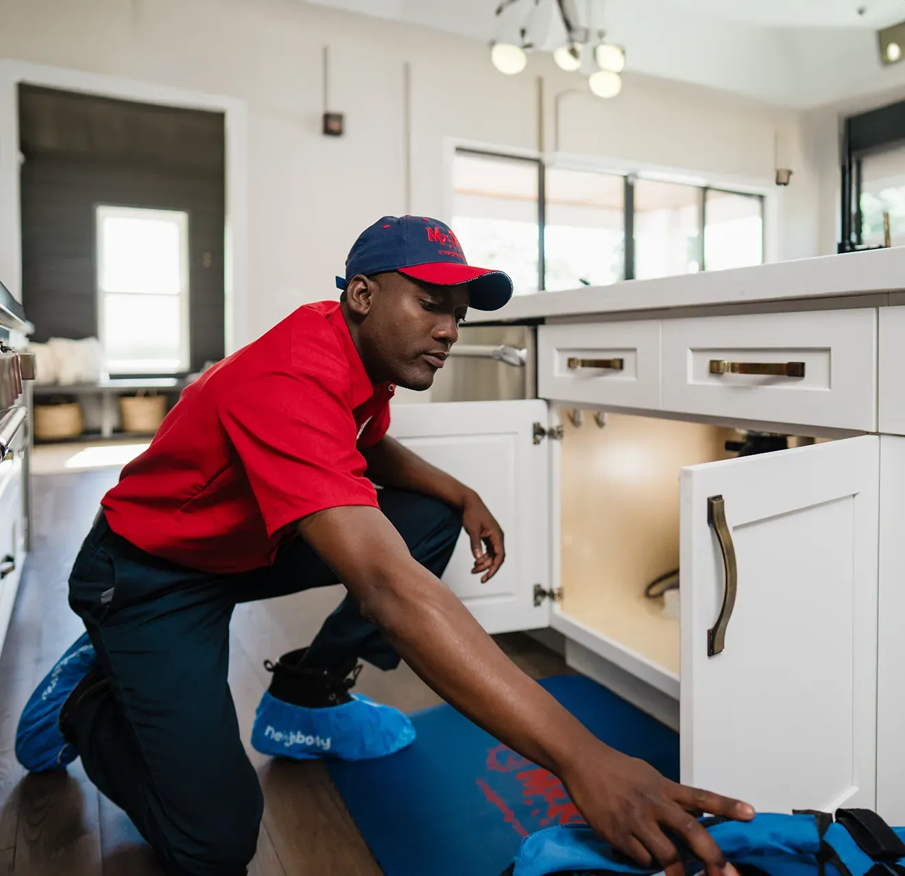 A professional wearing a red uniform and cap shows a tablet screen to a person while standing in a home.