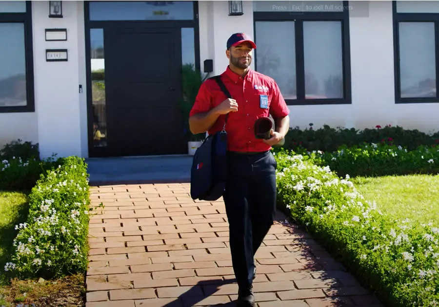 A professional wearing a red uniform and cap shows a tablet screen to a person while standing in a home.