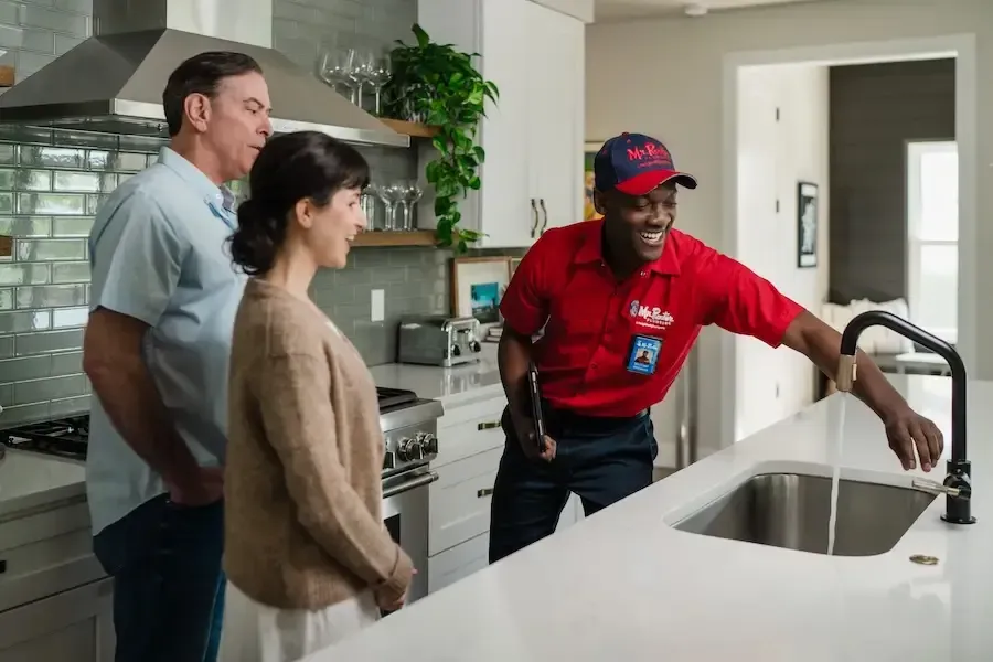 A professional wearing a red uniform and cap shows a tablet screen to a person while standing in a home.