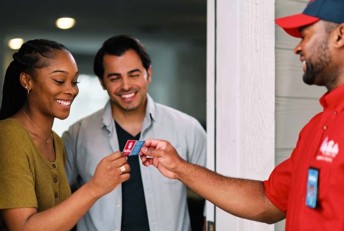 A professional wearing a red uniform and cap shows a tablet screen to a person while standing in a home.