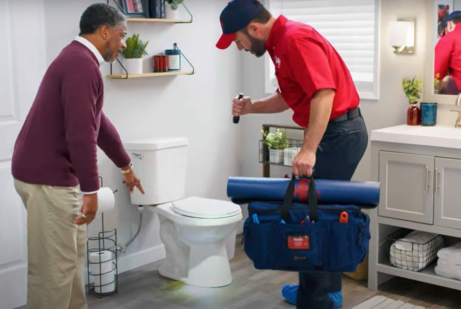 A professional wearing a red uniform and cap shows a tablet screen to a person while standing in a home.