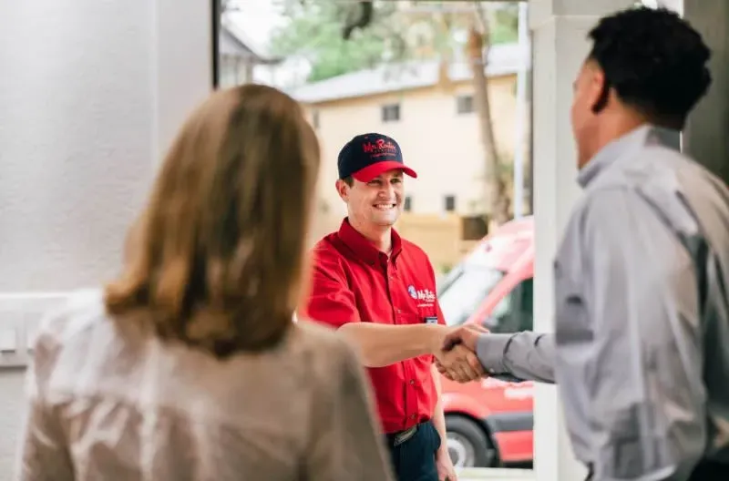 A professional wearing a red uniform and cap shows a tablet screen to a person while standing in a home.