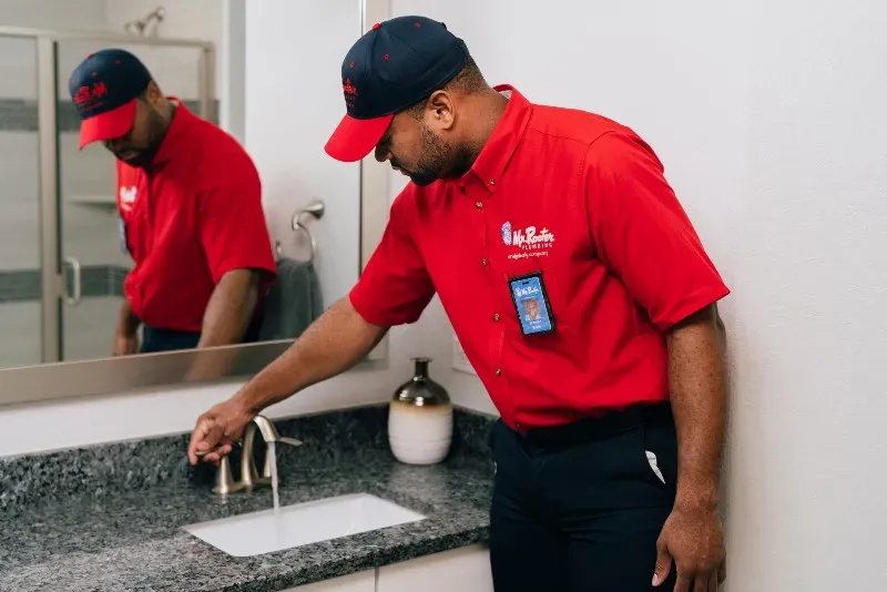 A professional wearing a red uniform and cap shows a tablet screen to a person while standing in a home.