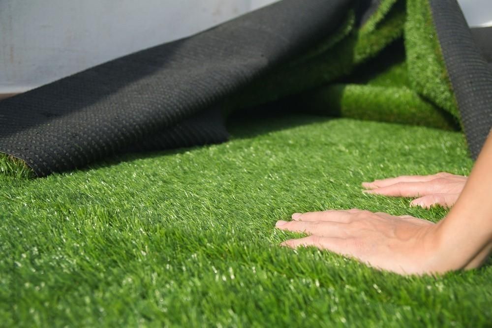a person is laying a roll of artificial grass on the ground .