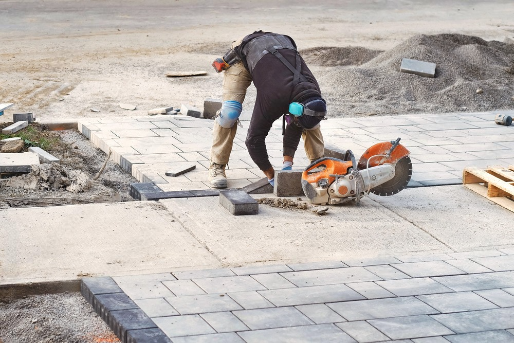 a man is using a circular saw to cut bricks on a sidewalk .