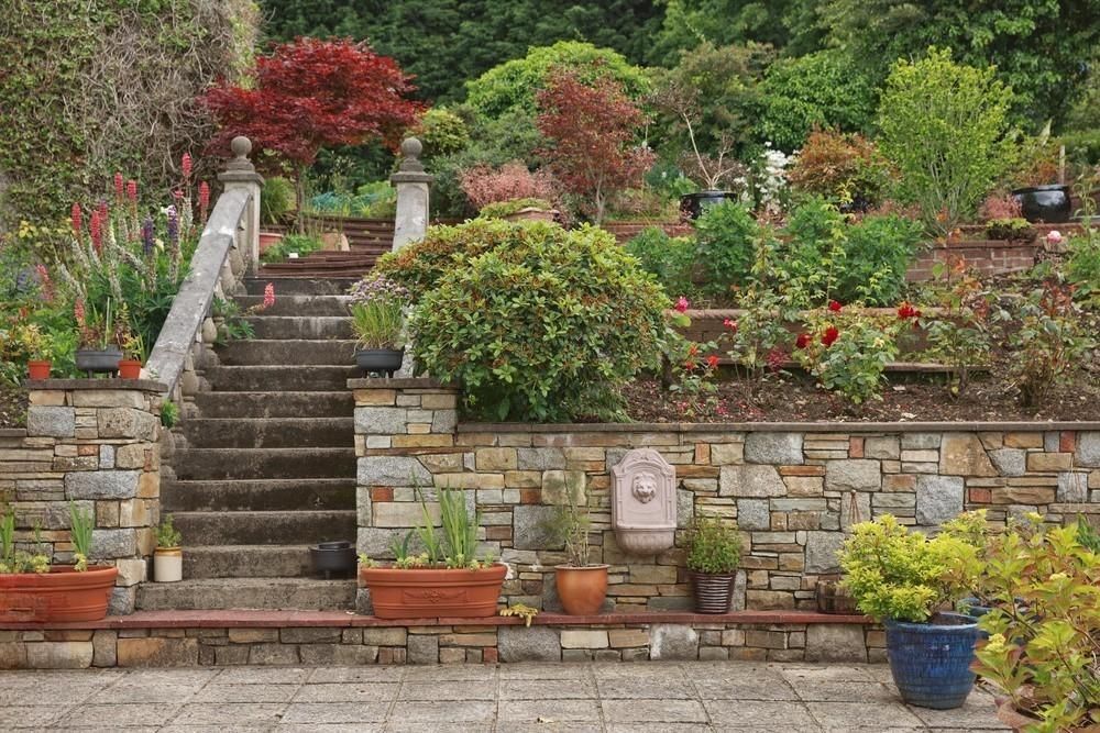 a stone wall is surrounded by potted plants and stairs in a garden .