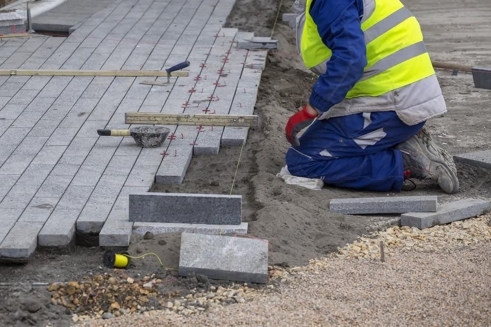 a construction worker is kneeling down while laying bricks on the ground .
