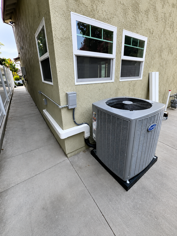 Outdoor HVAC unit beside beige house wall and windows on a concrete walkway
