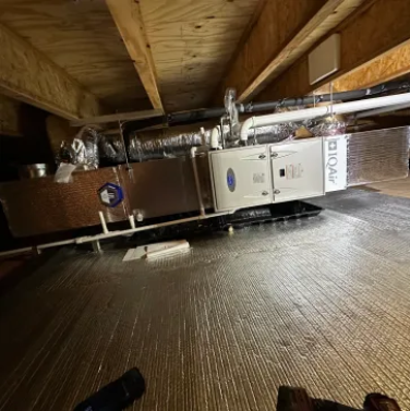 Attic HVAC unit and ductwork beneath a wooden roof with insulation on the floor