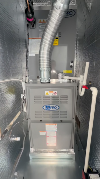 HVAC furnace unit in a narrow utility closet with silver ductwork and pipes along the walls