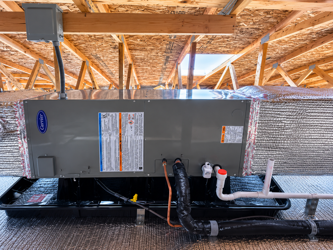 HVAC unit installed in a wooden attic, with ductwork and exposed roof framing above.