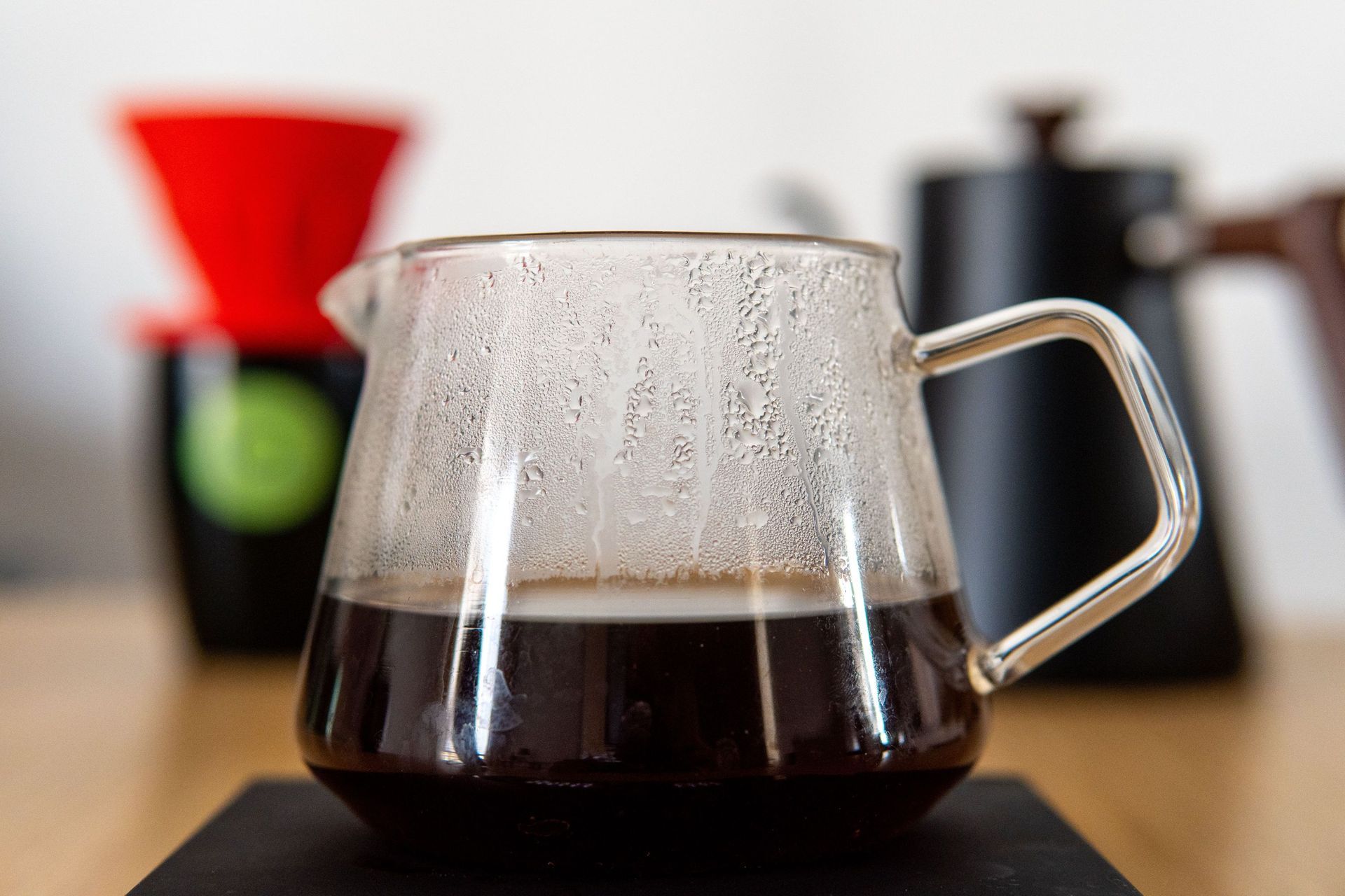 A clear glass server containing freshly brewed black coffee resting on a dark pad with a red dripper