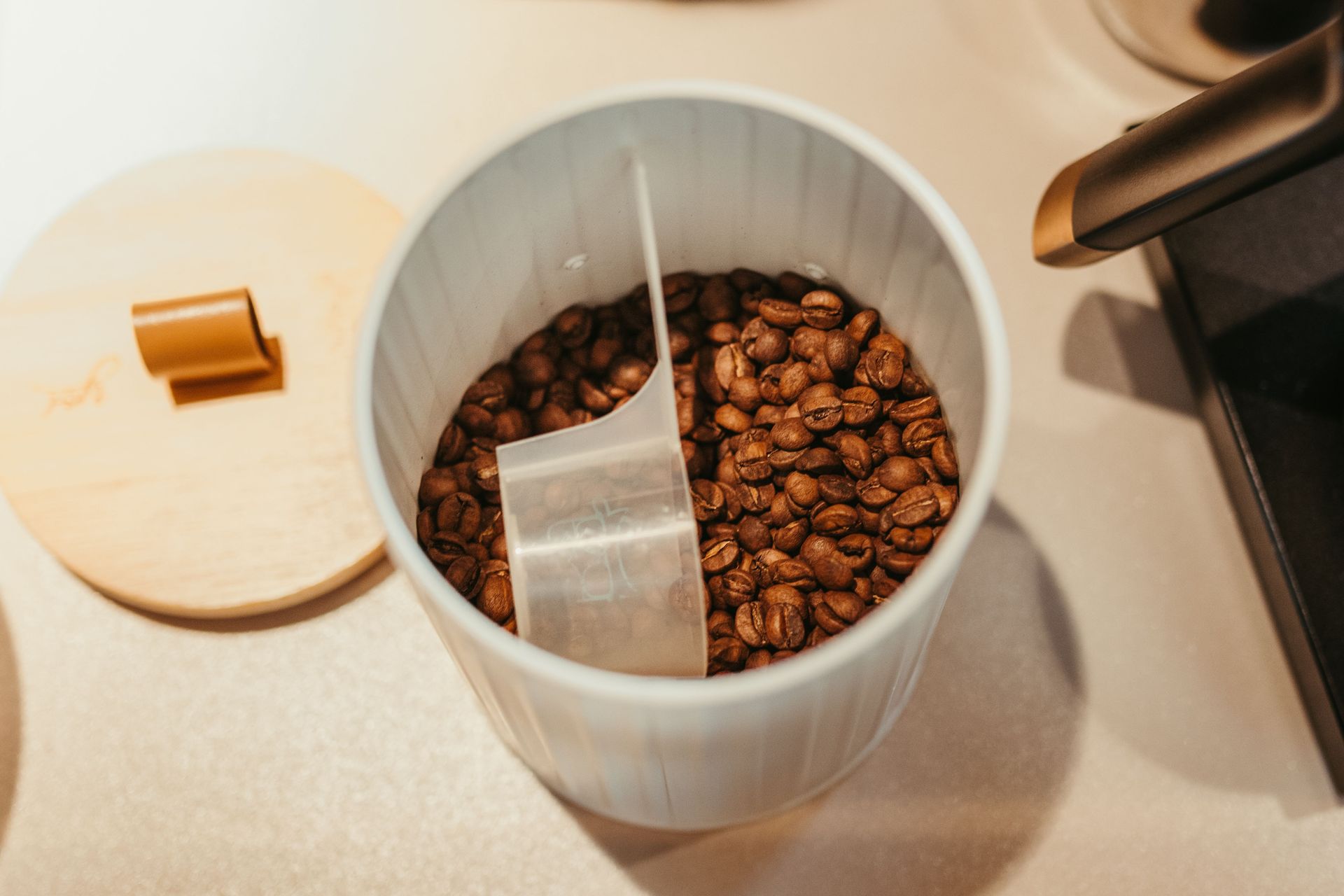 A top-down view showing a white container filled with roasted coffee beans and a plastic scoop sitting inside.
