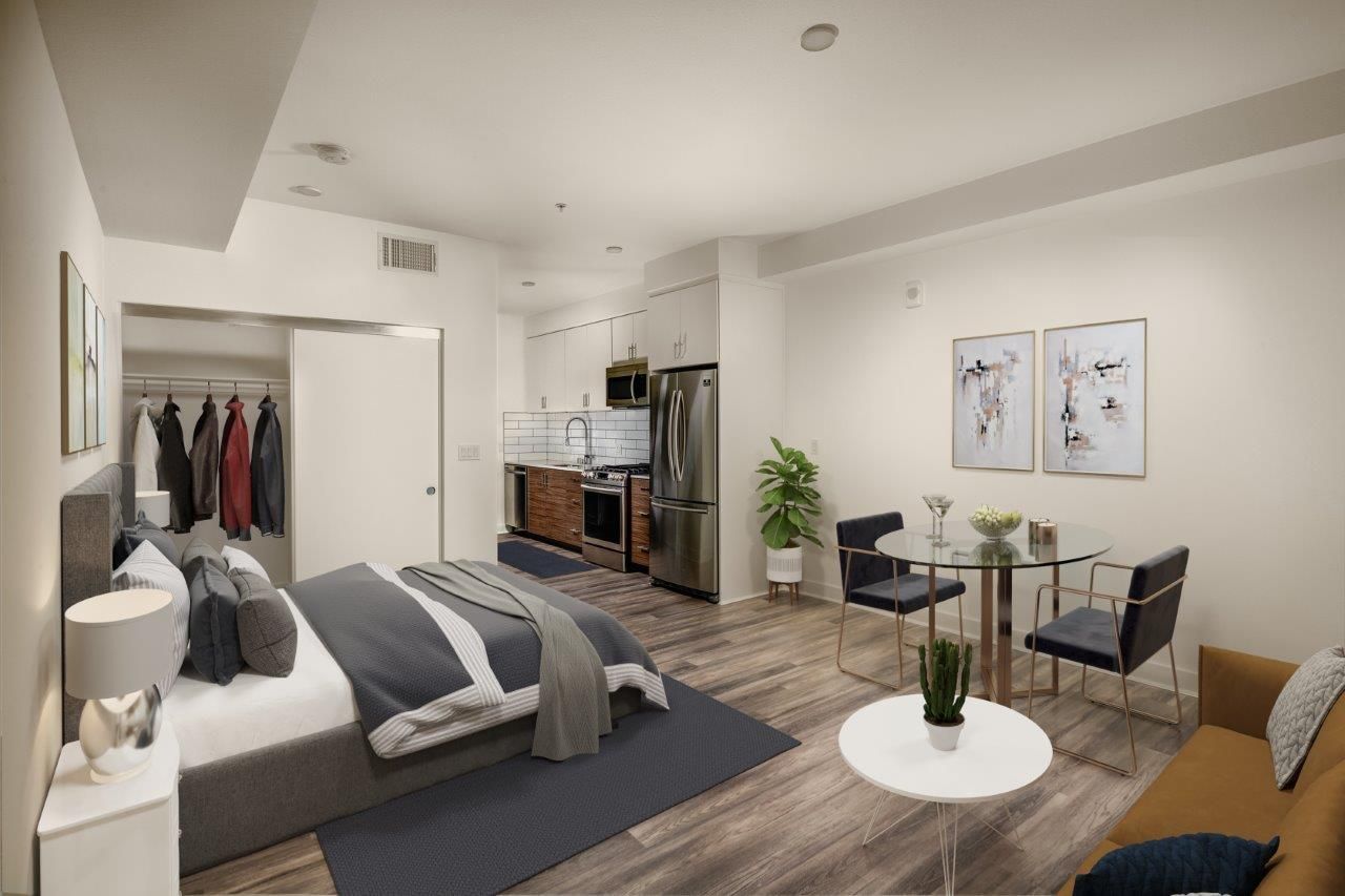 Studio apartment interior with bed, small kitchen, dining area, and sofa. Bright, neutral colors.