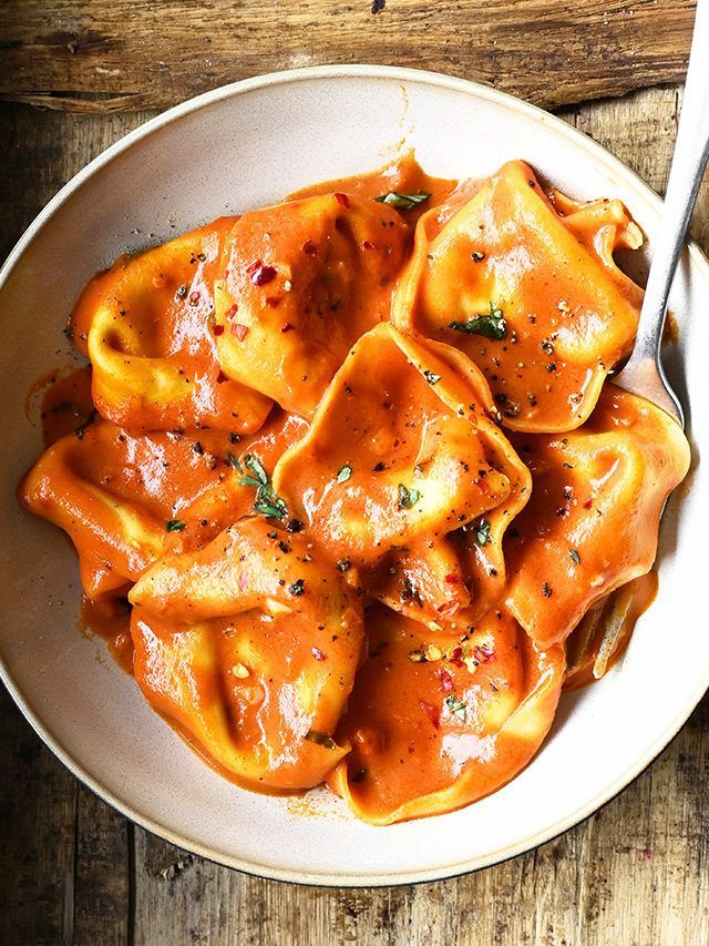 Creamy tomato tortellini topped with parmesan cheese served in a neutral-toned bowl on a kitchen counter.
