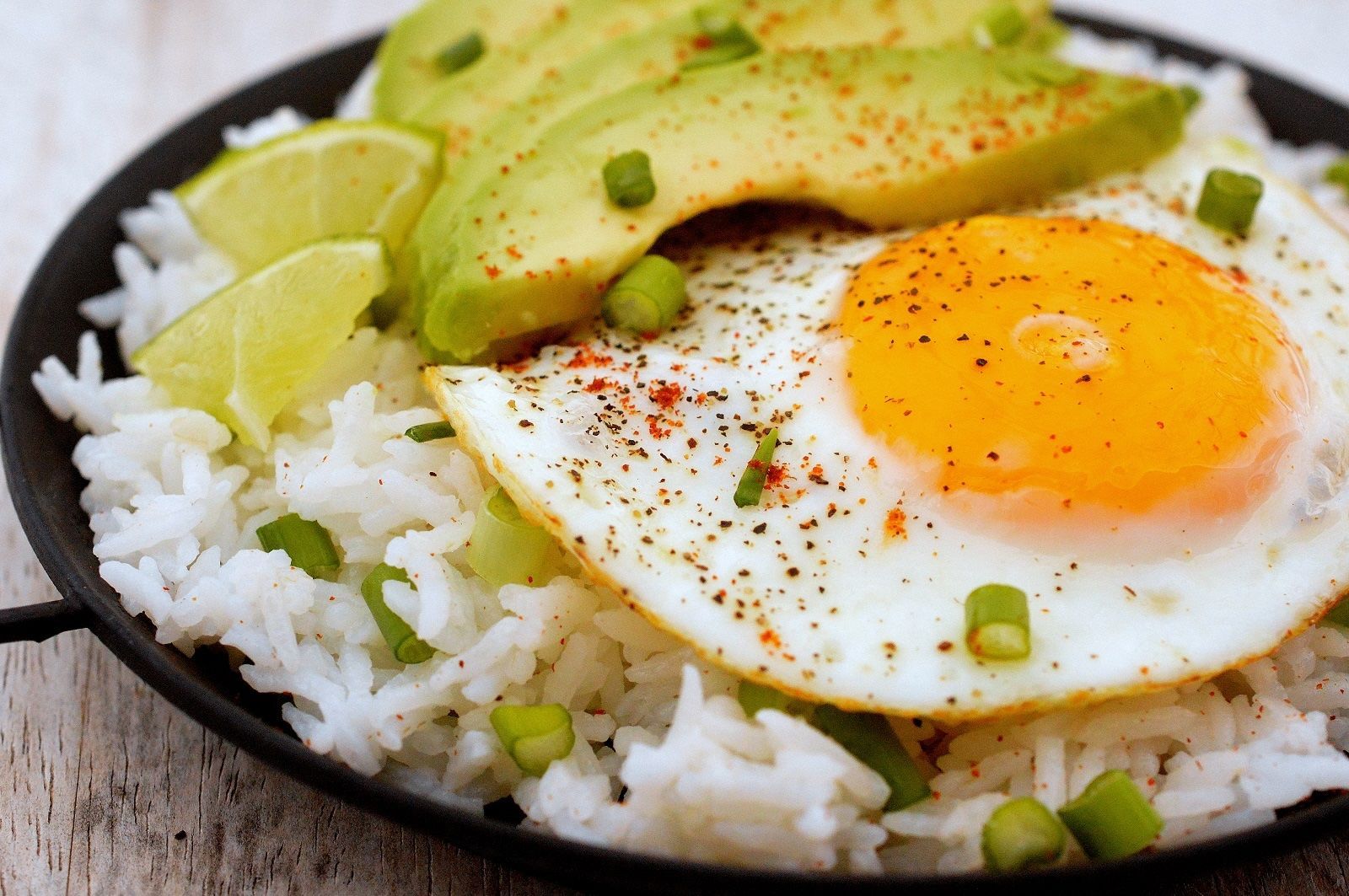 Fried egg rice bowl with sliced avocado, green onions, and chili flakes served in a simple ceramic bowl.