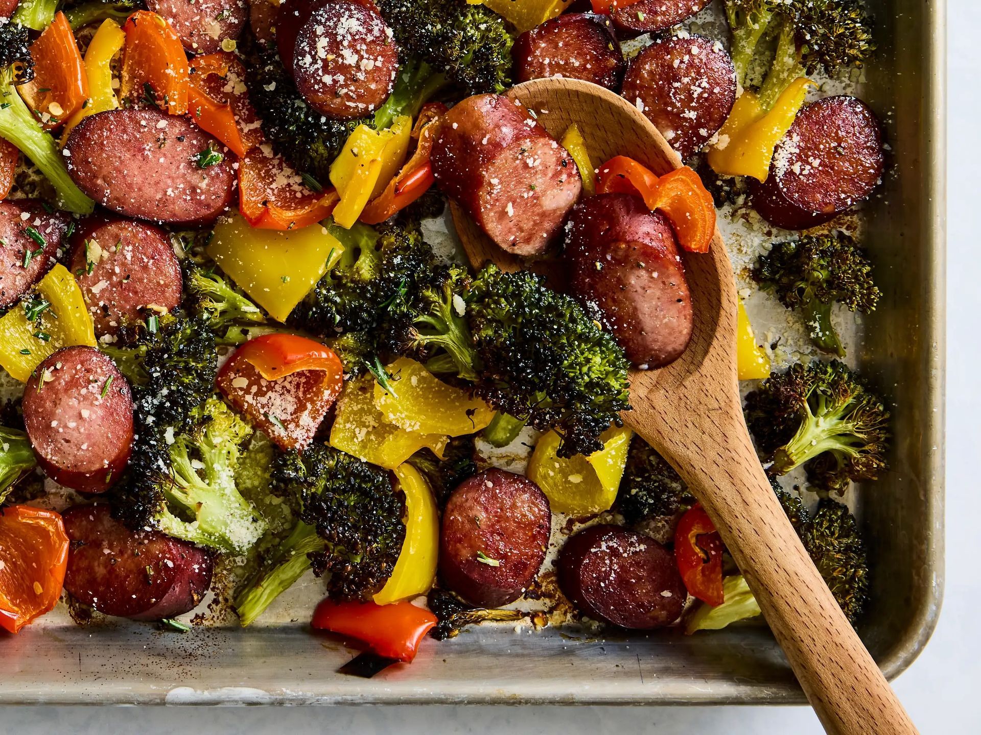 Sheet pan roasted sausage with bell peppers and zucchini arranged in a rustic oven tray.