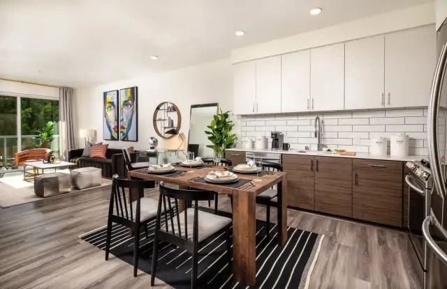 A kitchen and dining area in an apartment at The Ovelo Hollywood featuring white and wood cabinets