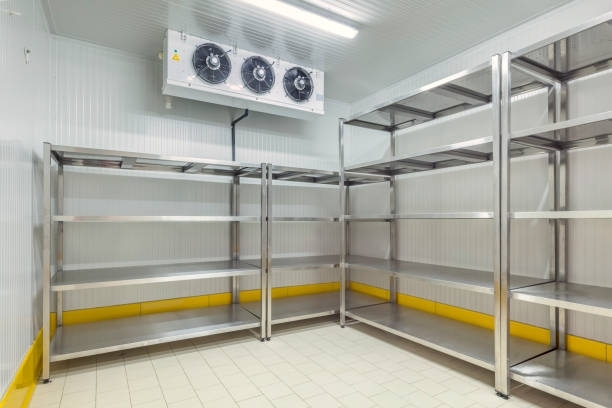 Empty commercial walk-in refrigerator with stainless steel shelving. Ceiling-mounted cooling unit above.