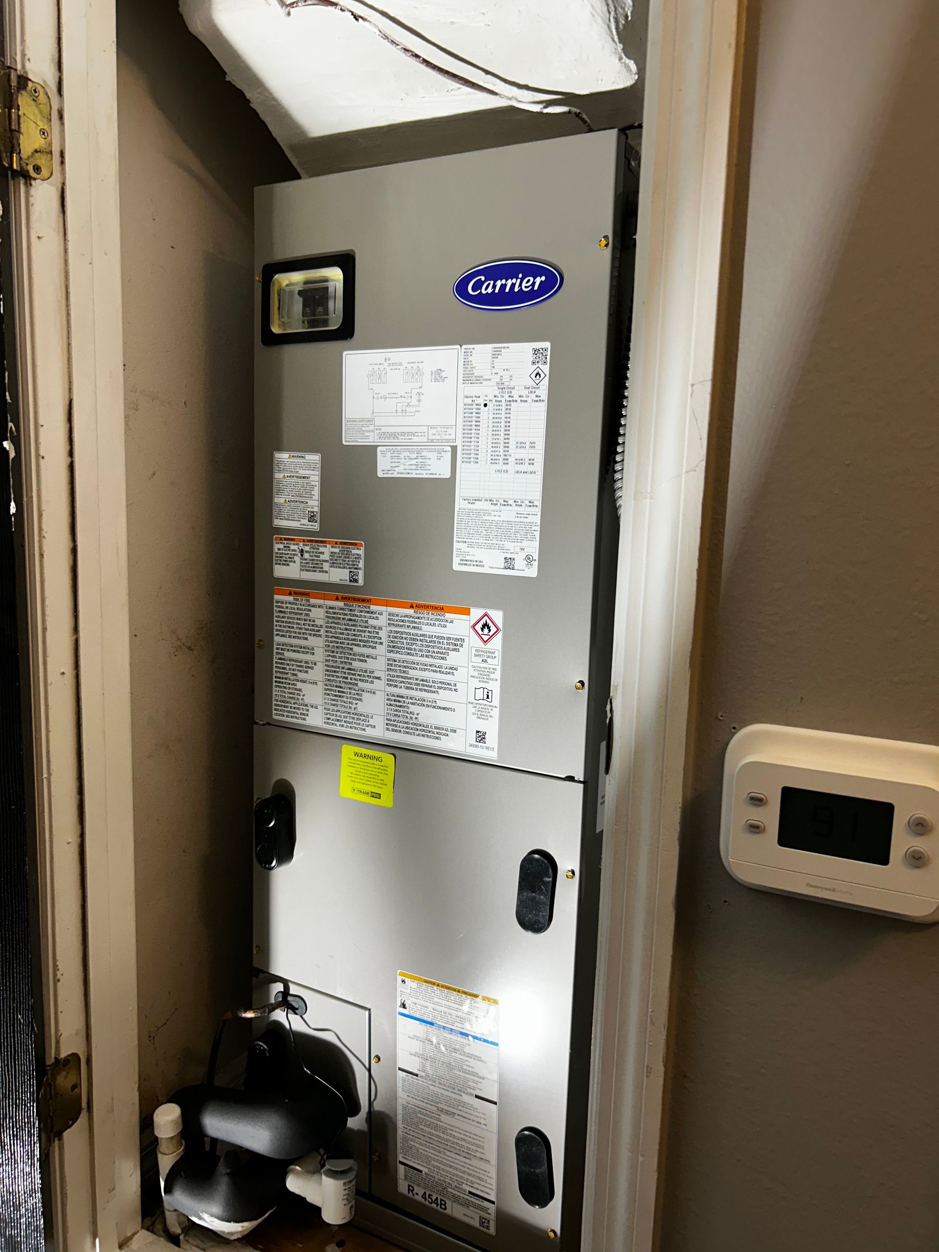 Gray furnace/air handler in a narrow utility closet with a wall thermostat on the right.