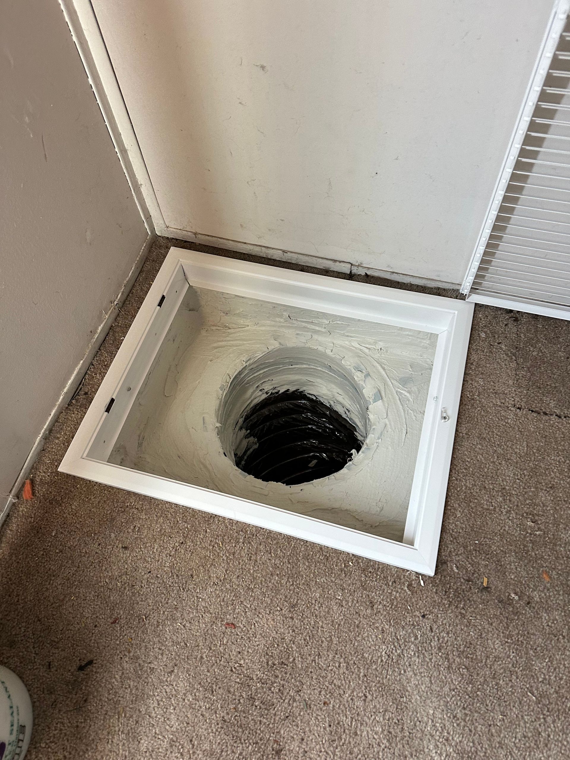 Open floor vent with a white frame in a carpeted corner by the wall