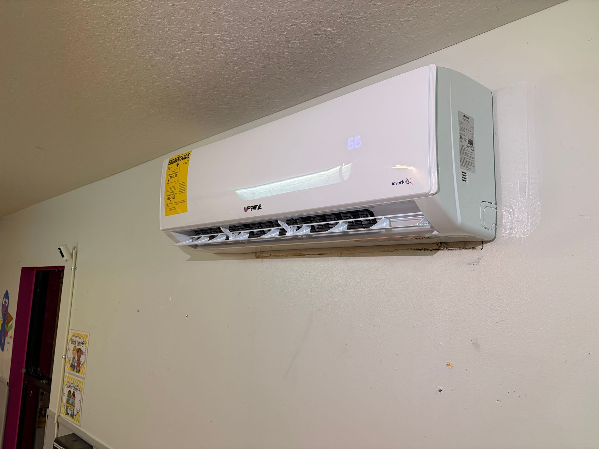 White wall-mounted air conditioner with open vents on a beige wall near the ceiling.