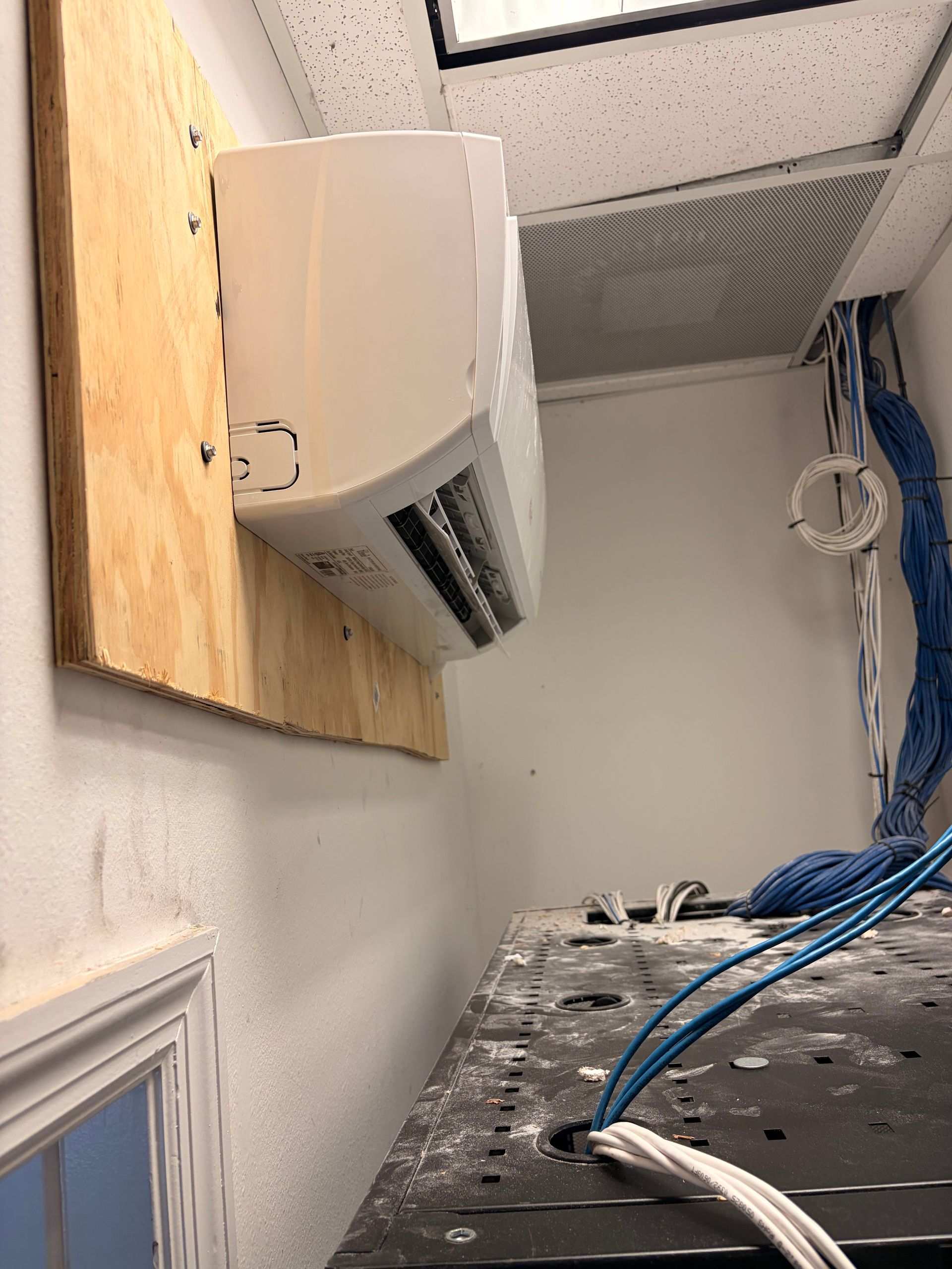 Wall-mounted air conditioner above a cluttered workspace with blue cables and dust on a counter