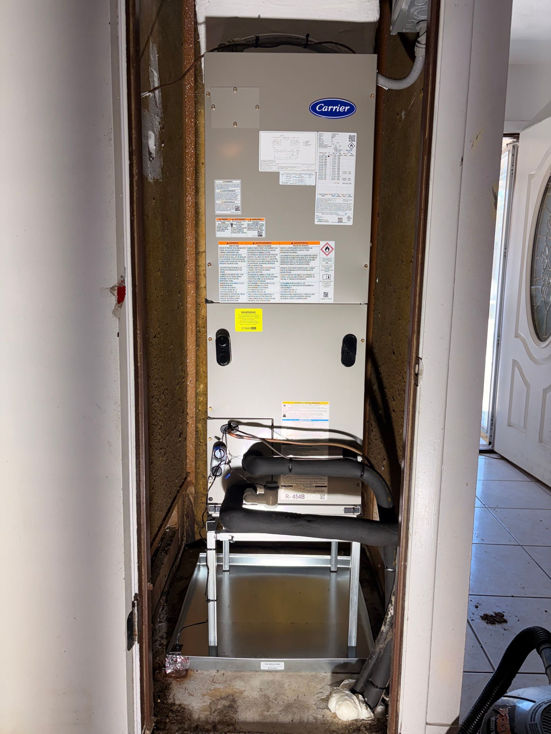 HVAC furnace in a narrow closet opening, with a metal dolly in front and drywall exposed around it
