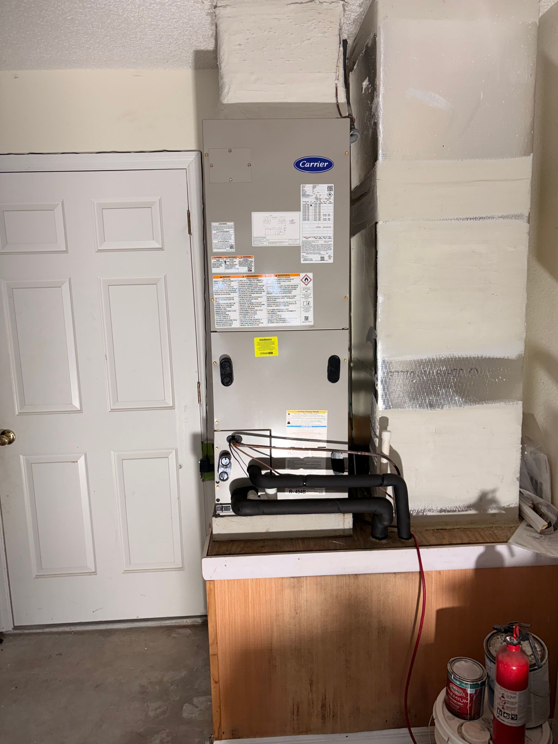 HVAC unit beside a white door, with red fire extinguishers and pipes in a utility room