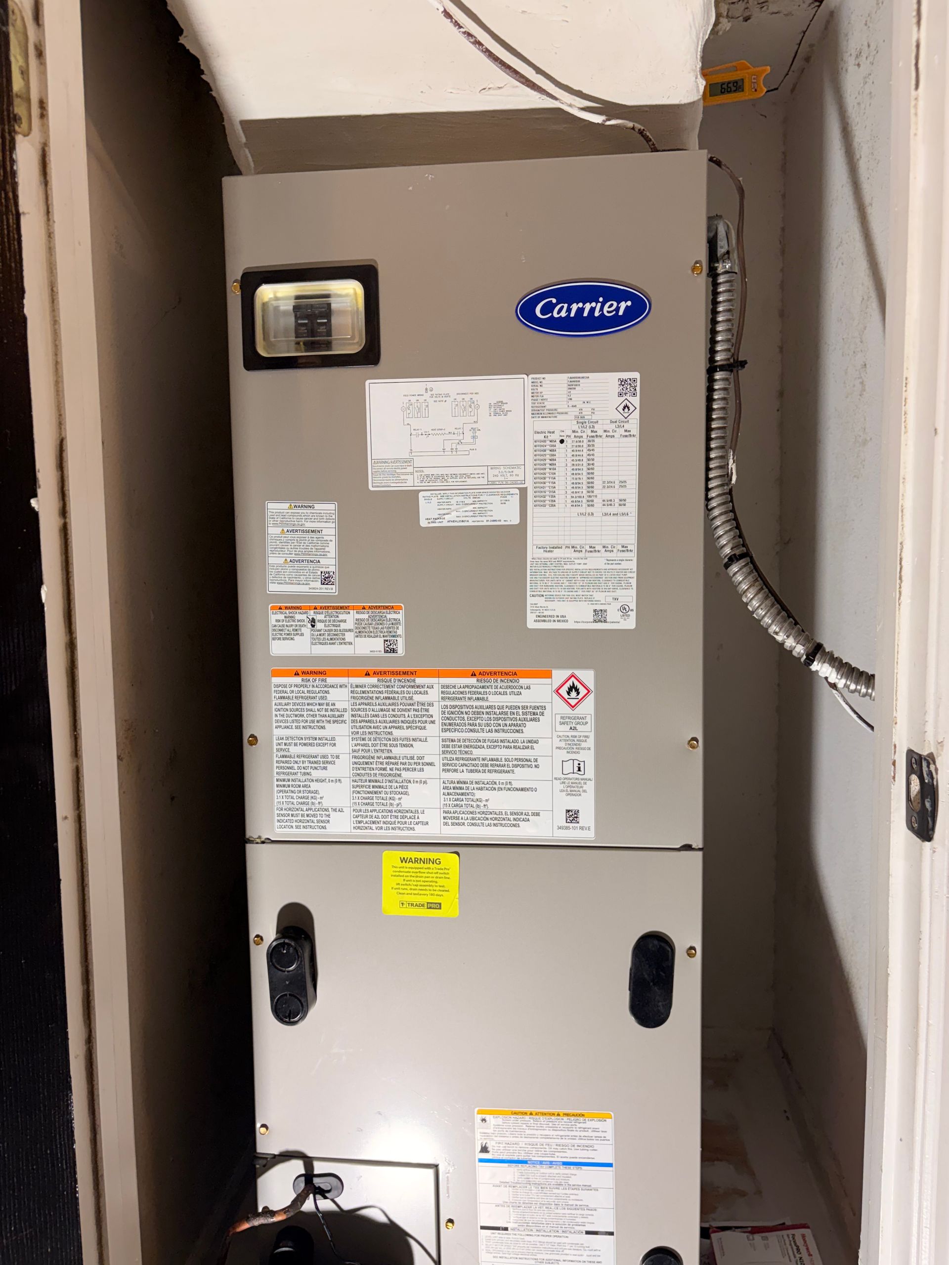 Carrier HVAC unit in a narrow utility closet with labels and conduit attached