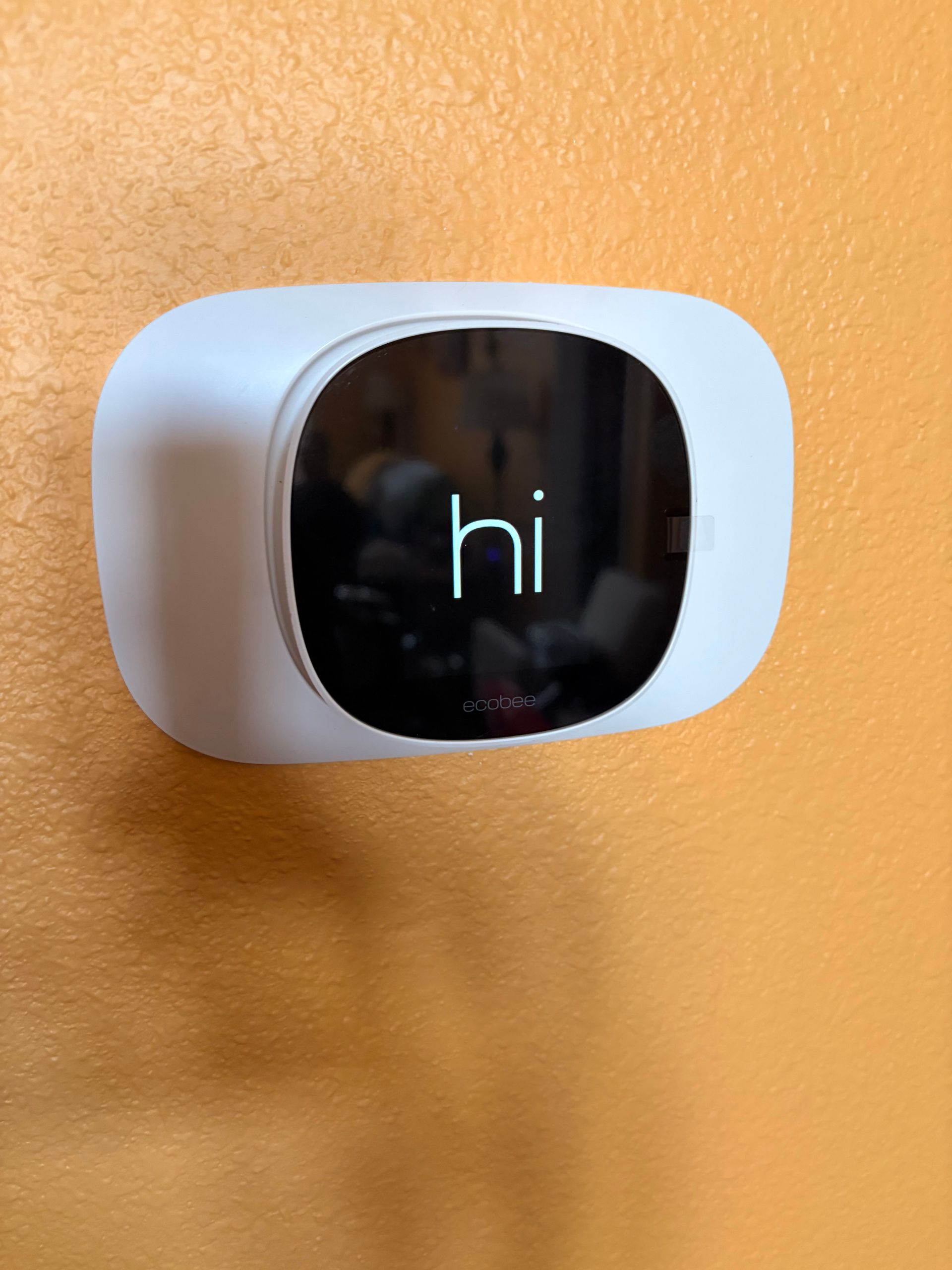 White wall-mounted device with a black screen displaying “hi” against an orange wall