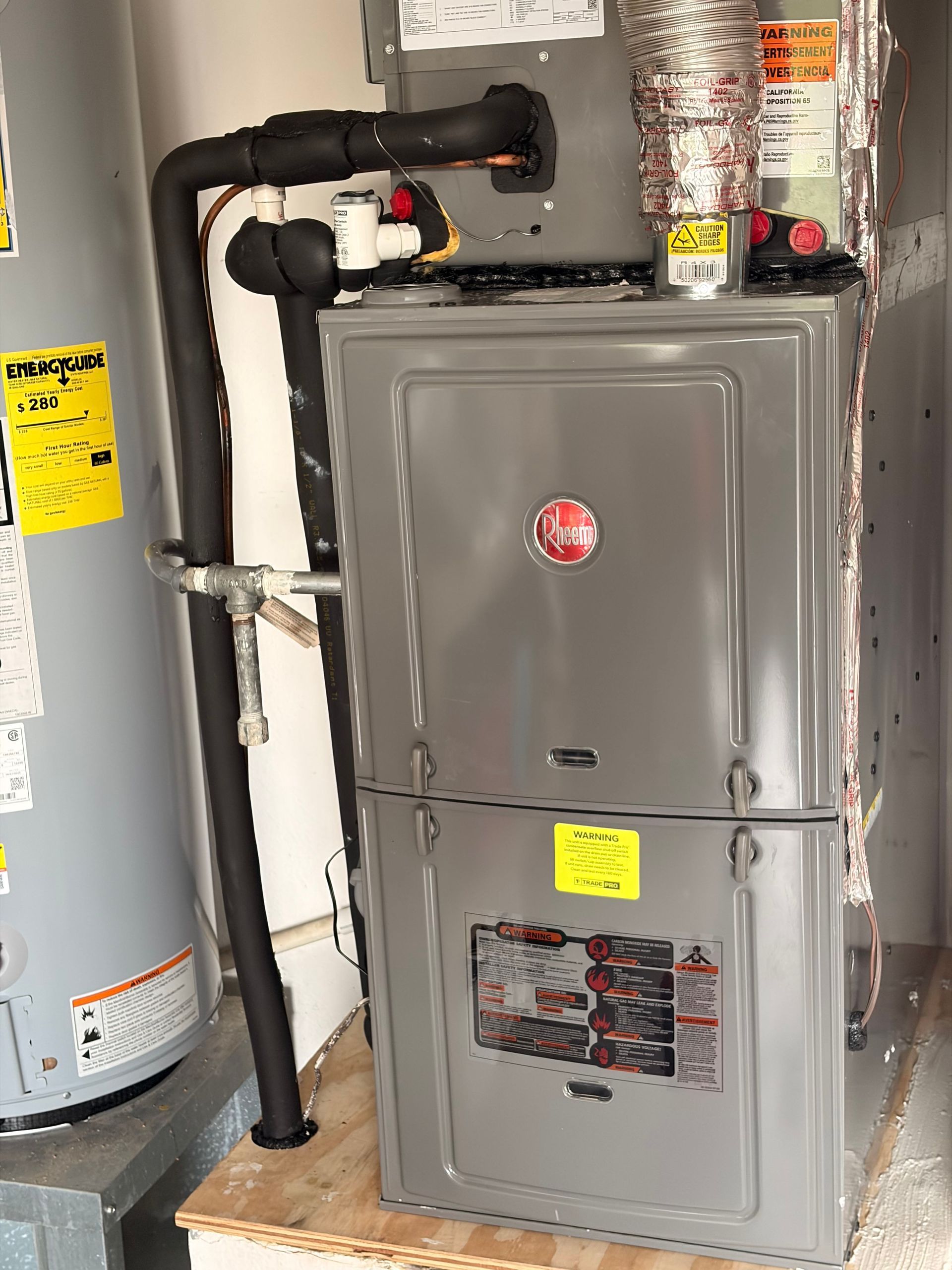 Gray furnace in a utility room with exposed pipes and ductwork beside a water heater.