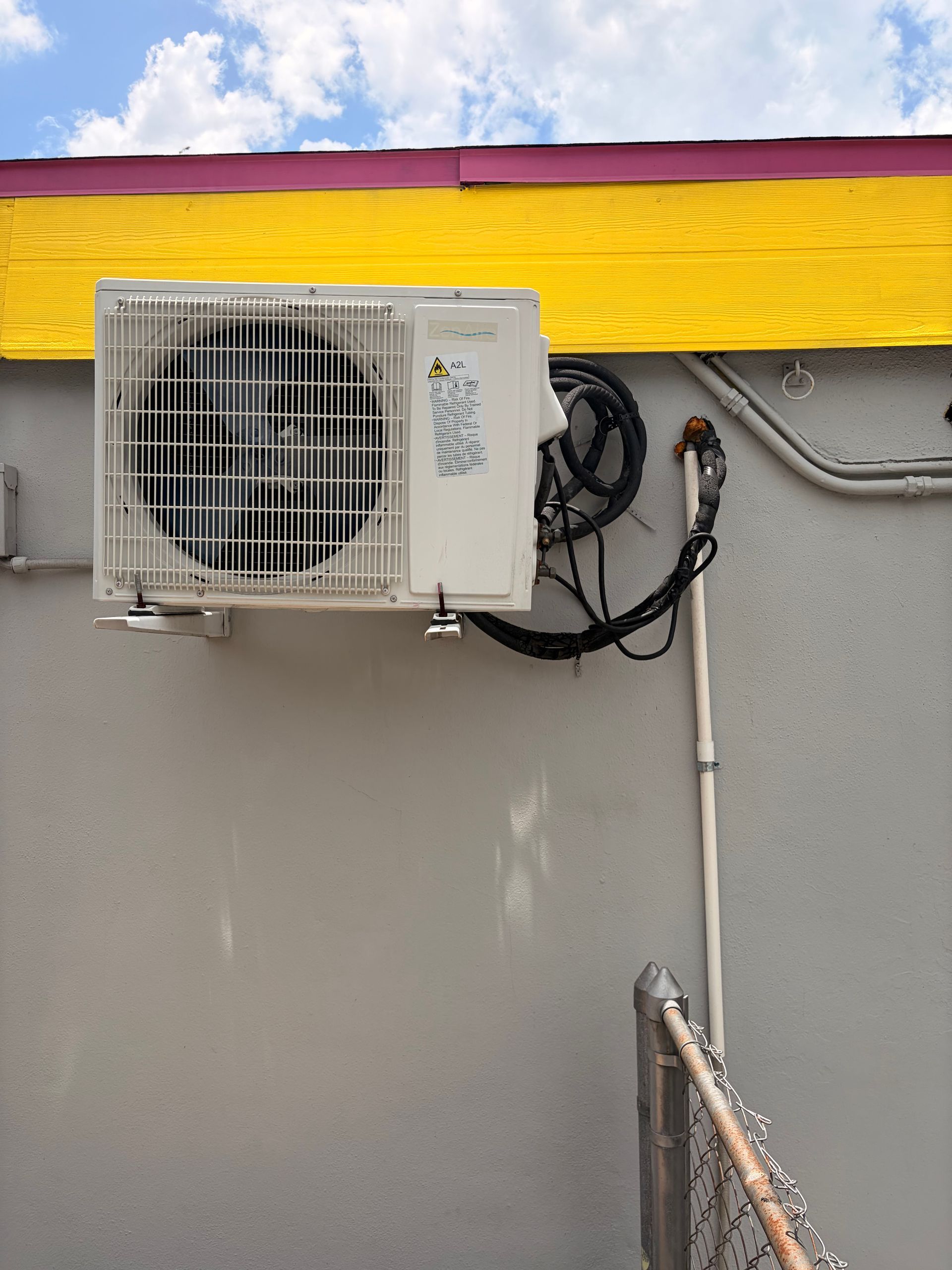 Wall-mounted air conditioner unit on a gray exterior wall with yellow trim and blue sky above