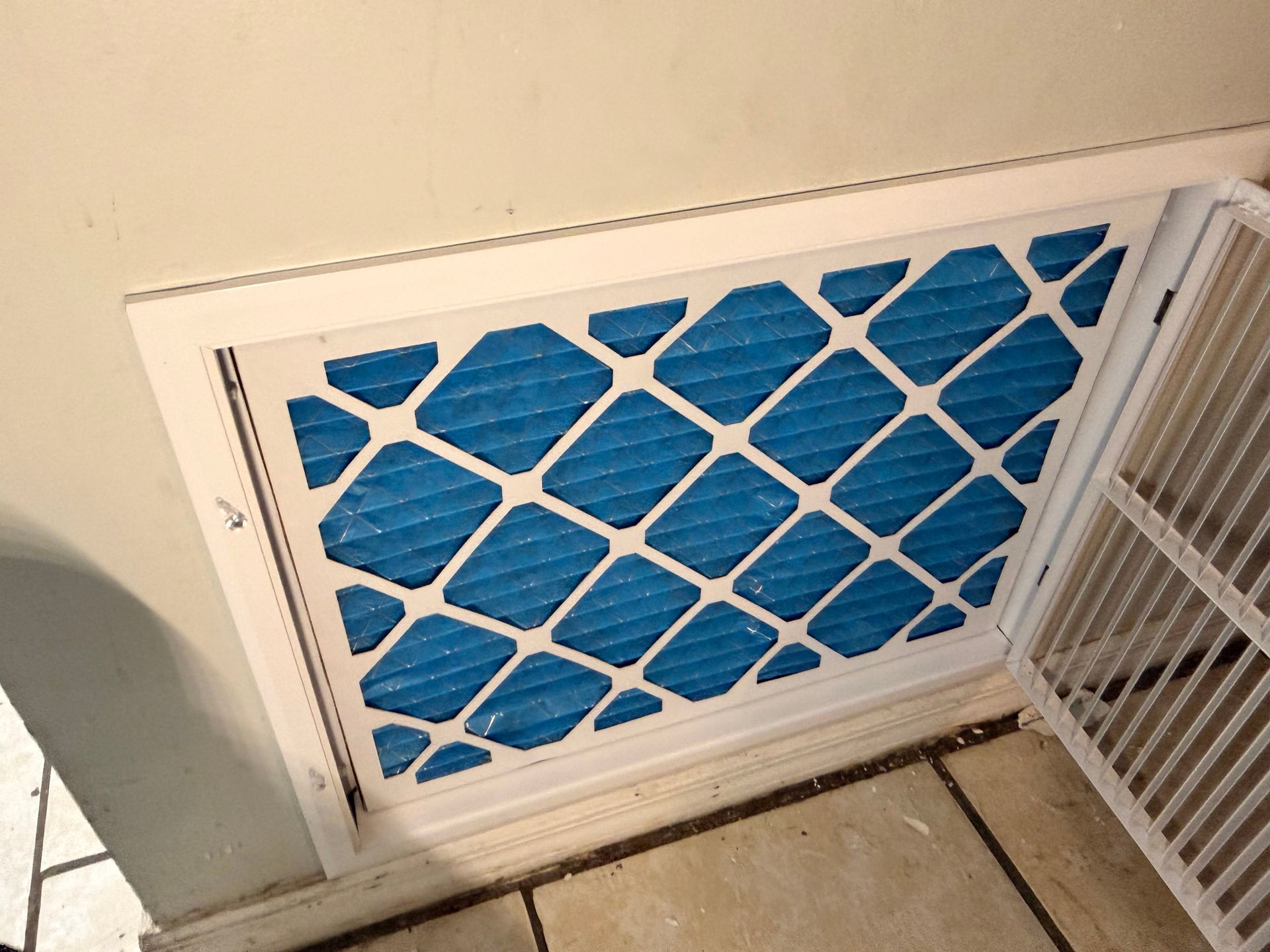 Blue HVAC return vent with white frame and filter grid near the floor.