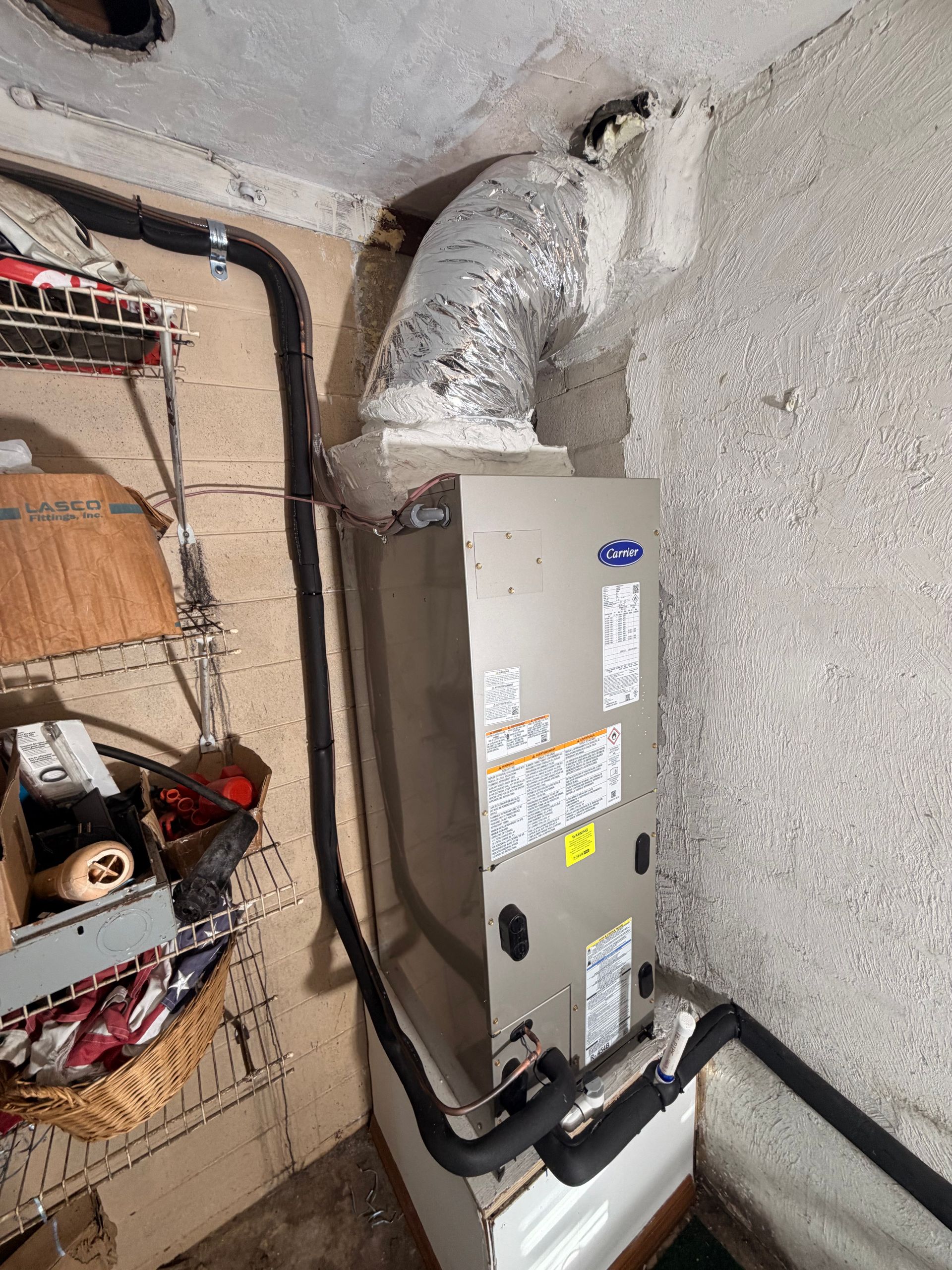 Basement utility closet with a gray HVAC unit, exposed piping, and electrical wiring on concrete walls