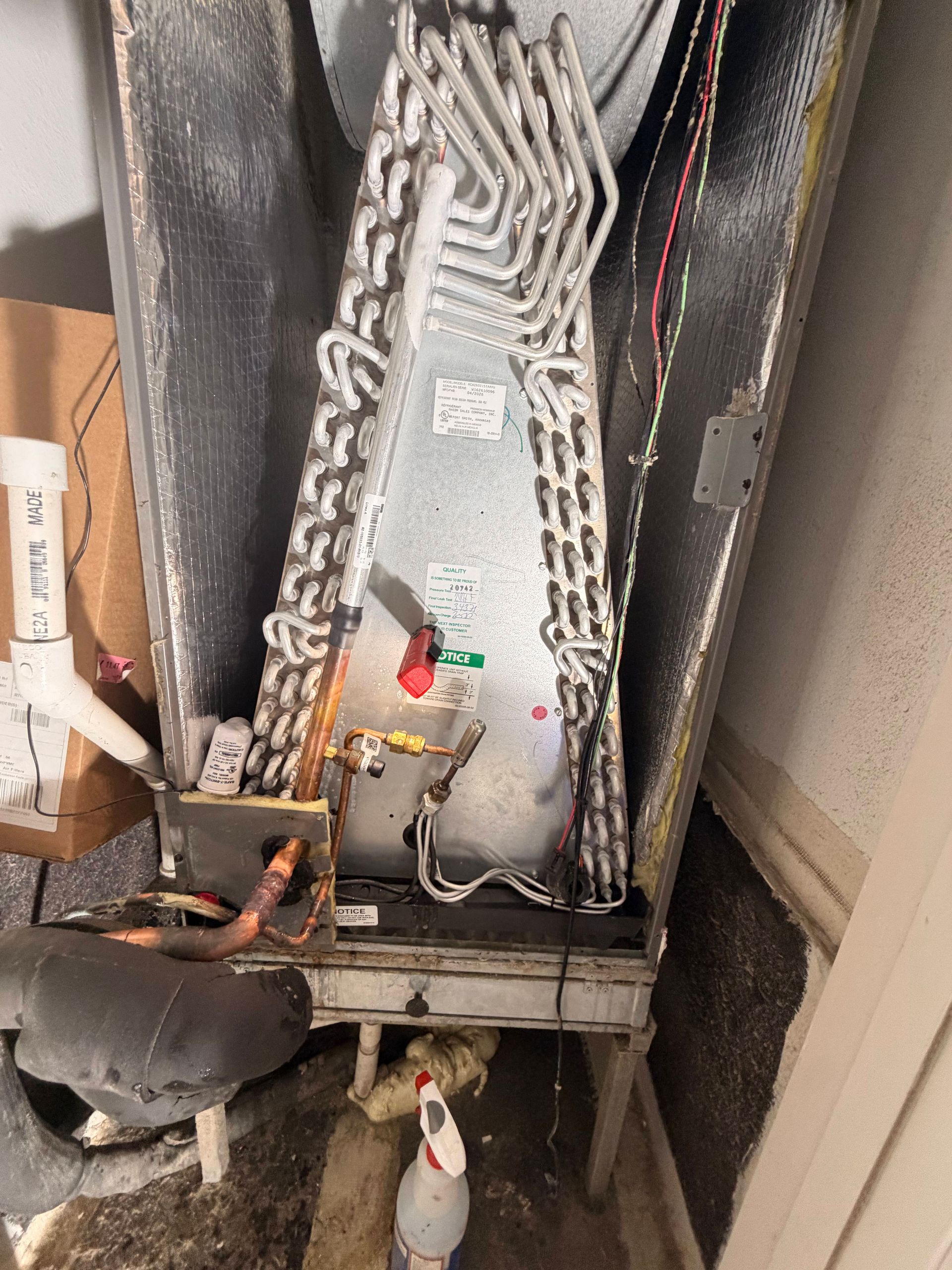 Air conditioner unit and ductwork on a porch, with a fan and bottles below.