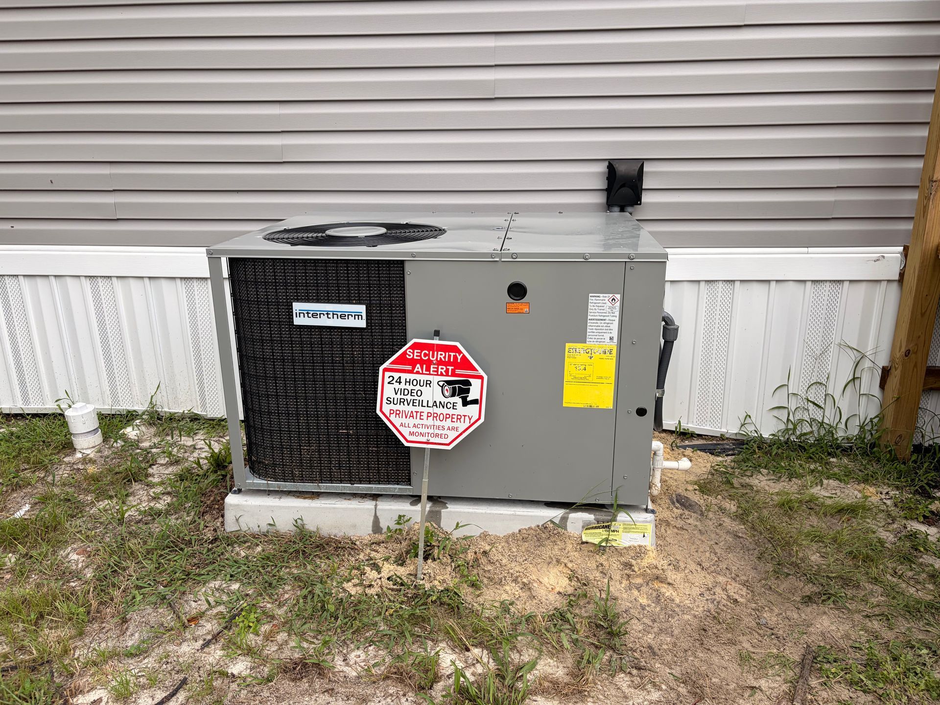 Outdoor HVAC unit beside a house, with warning labels on the front and side.